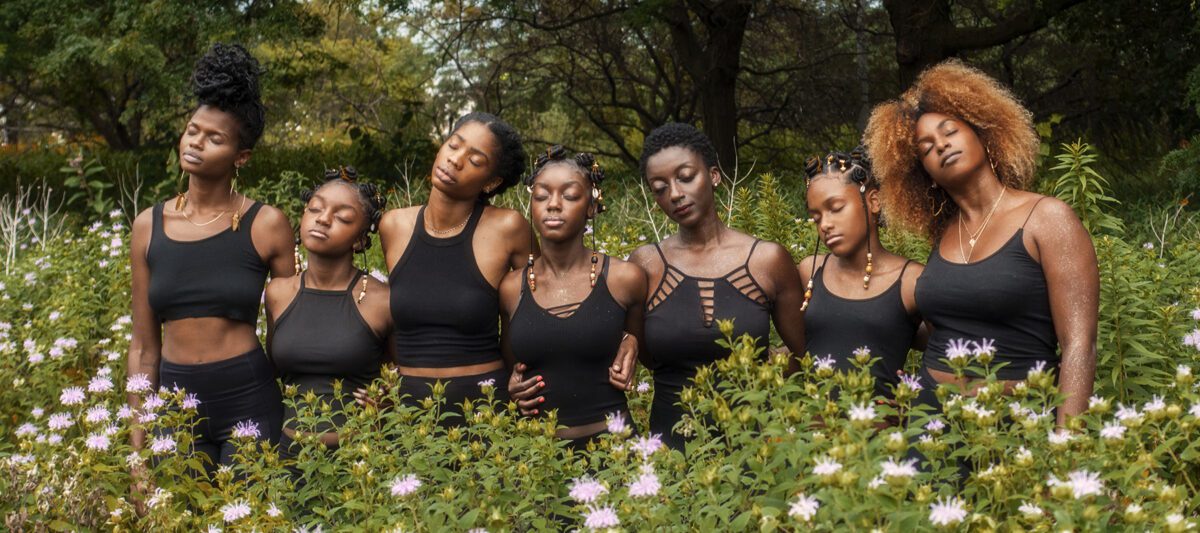 Seven black women of varying ages stand together in a field of flowers